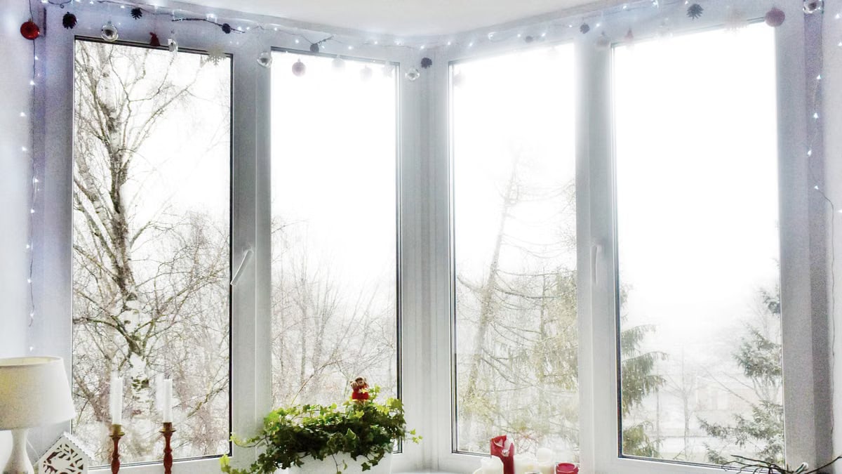 A bright winter window adorned with Christmas lights and decorations, creating a cozy festive atmosphere.
